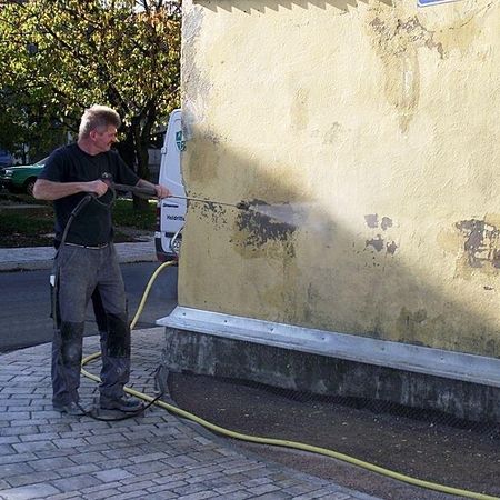 Intensivreinigung Gebäude mit Hochdruckreiniger an einer gelblichen Hausfassade an einer Straßenecke